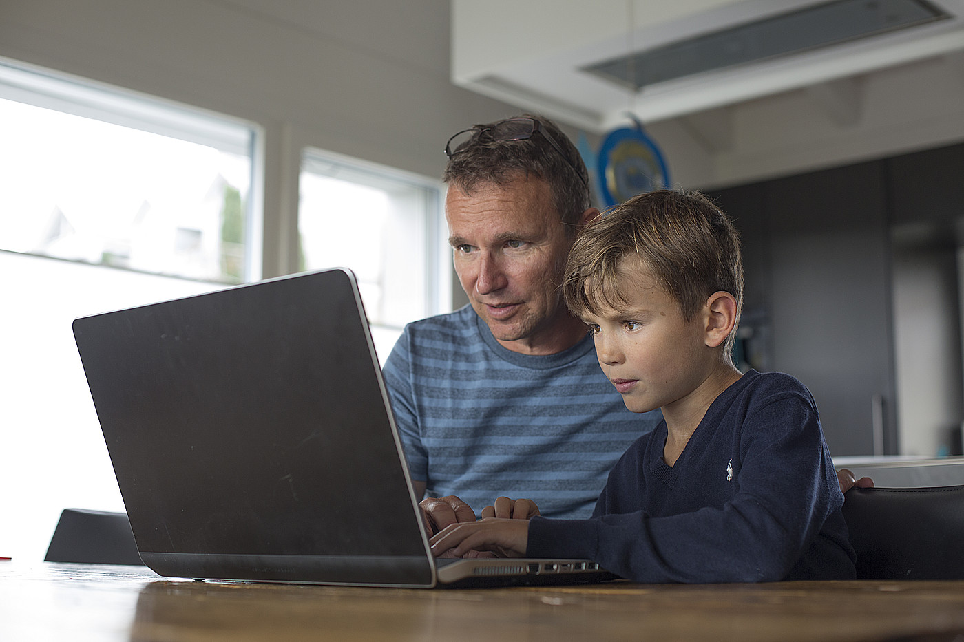 Ein Vater und ein Kind die gemeinsam auf einen Laptop schauen.
