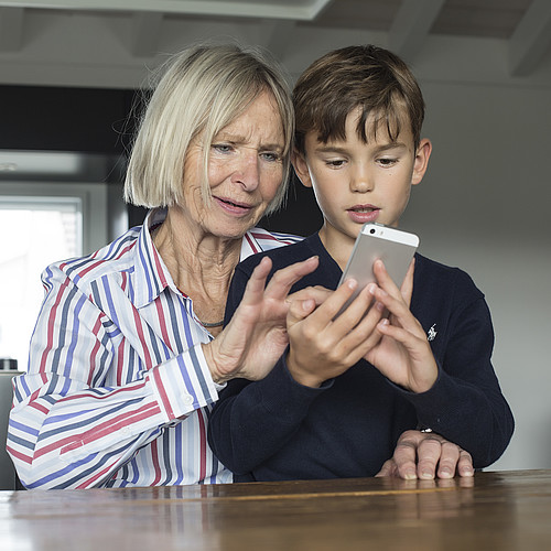 Eine ältere Frau zeigt einem kleinen Jungen die Benützung des Smartphones.