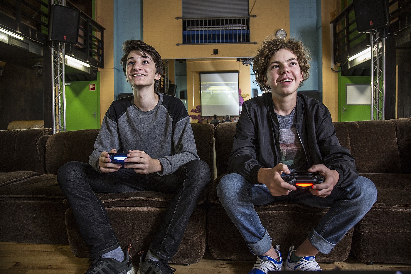 Zwei Jugendliche die auf einem Sofa in einem Jugendtreff sitzen und gemeinsam ein Videospiel spielen.