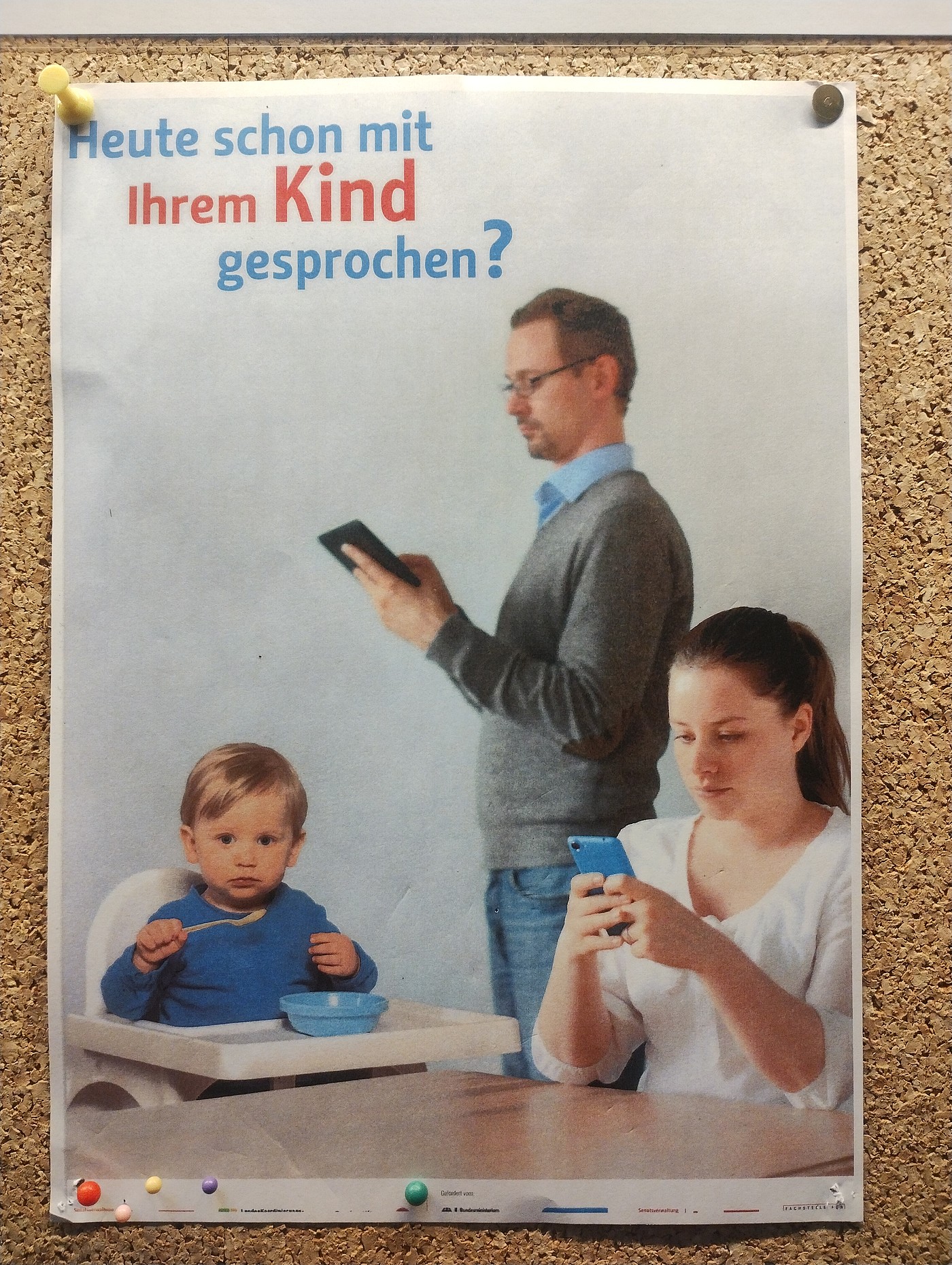 Vater und Mutter schauen auf ihr Handy, während das Kind isst und verdutzt in die Kamera schaut.