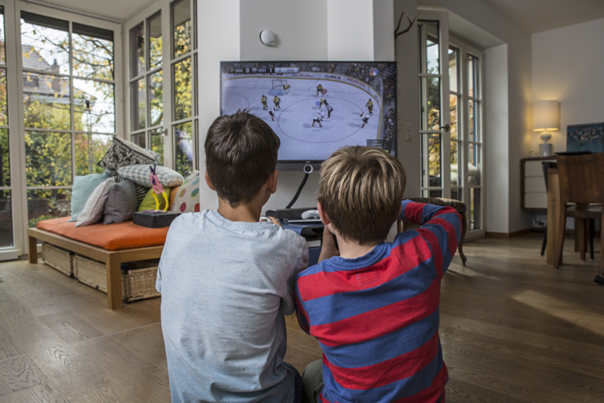 Zwei Kinder die gemeinsam auf dem Fernseher ein Eishockeygame spielen.