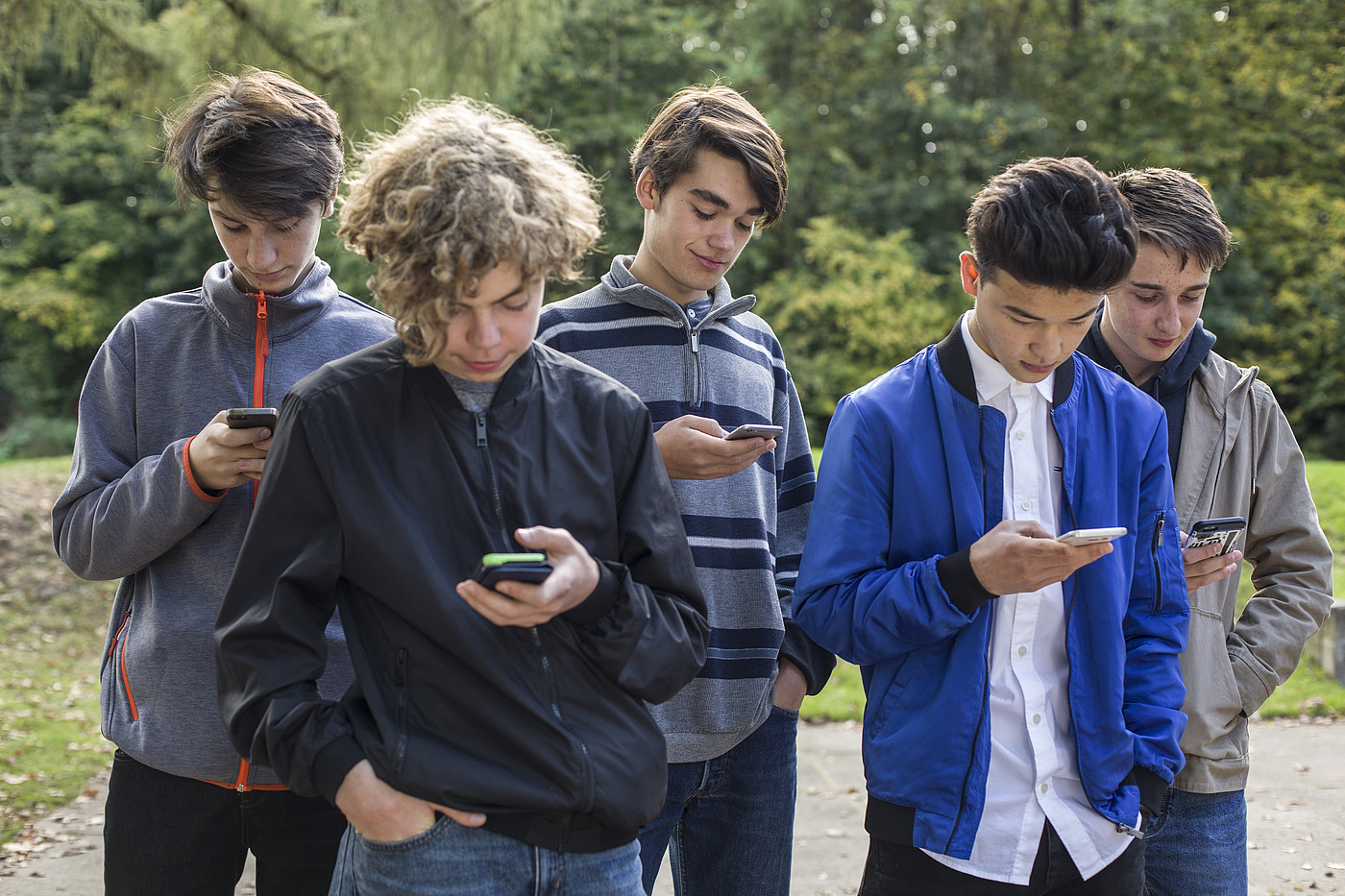 Fünf Jugendliche die draussen Stehen und alle auf ihr Smartphone schauen.
