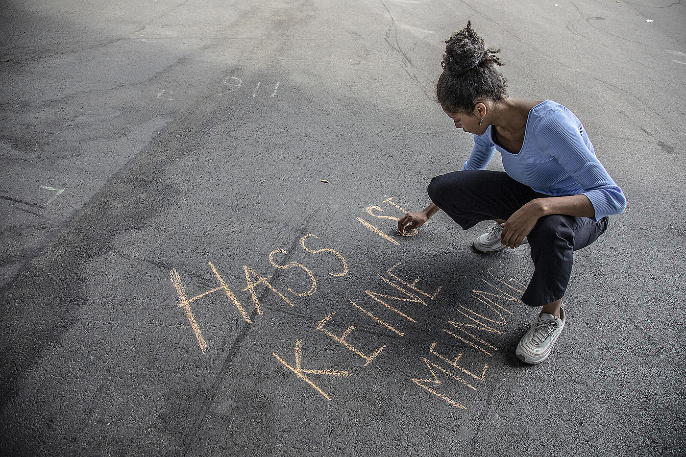 Eine Jugendliche schreibt mit Kreide "Hass ist keine Meinung" auf den Boden