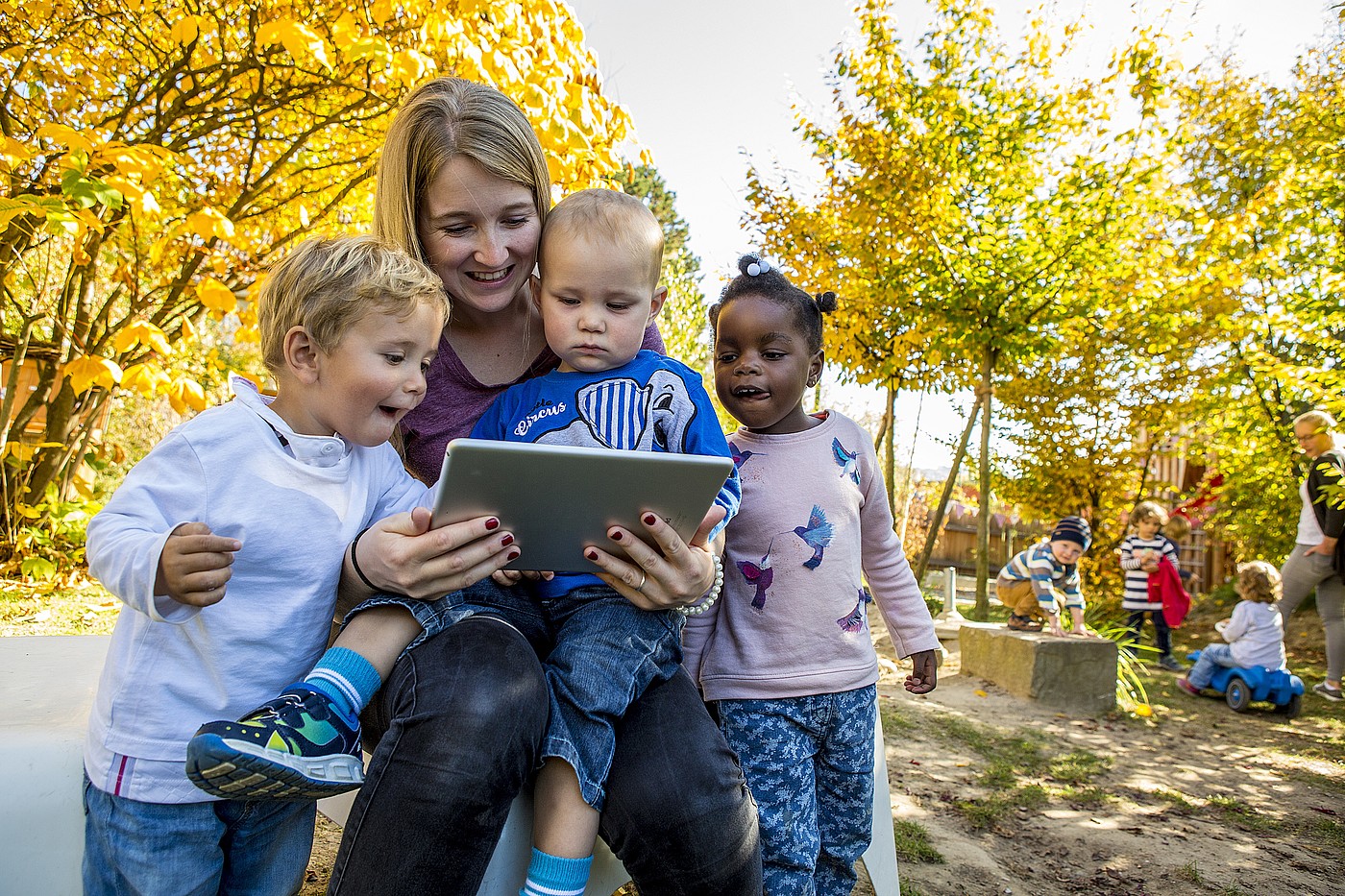 Eine Kinderbetreuerin schaut etwas mit den Kindern auf dem Tablet.