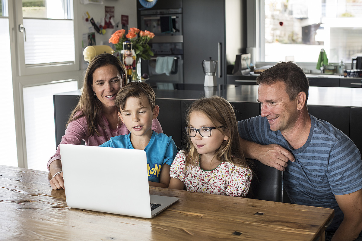 Die Eltern schauen mit ihrer Tochter und ihrem Sohn etwas auf dem Laptop an.