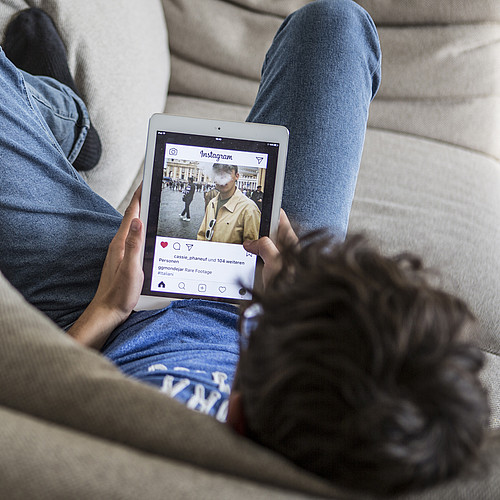 Ein Jugendlicher der auf dem Sofa liegt und auf dem Tablet Instagram geöffnet hat.