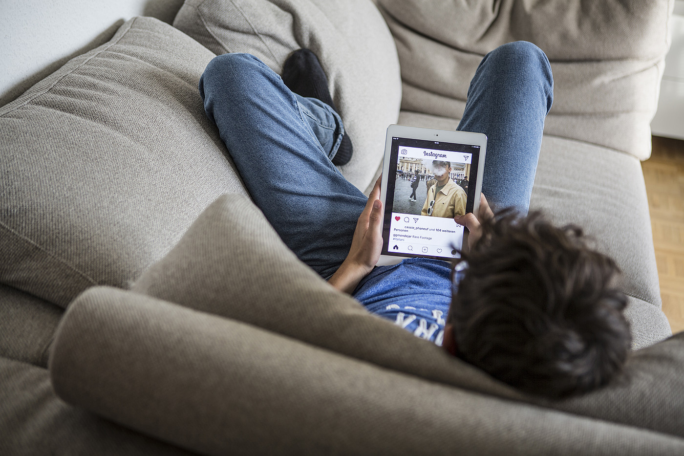 Ein Jugendlicher der auf dem Sofa liegt und auf dem Tablet Instagram geöffnet hat.