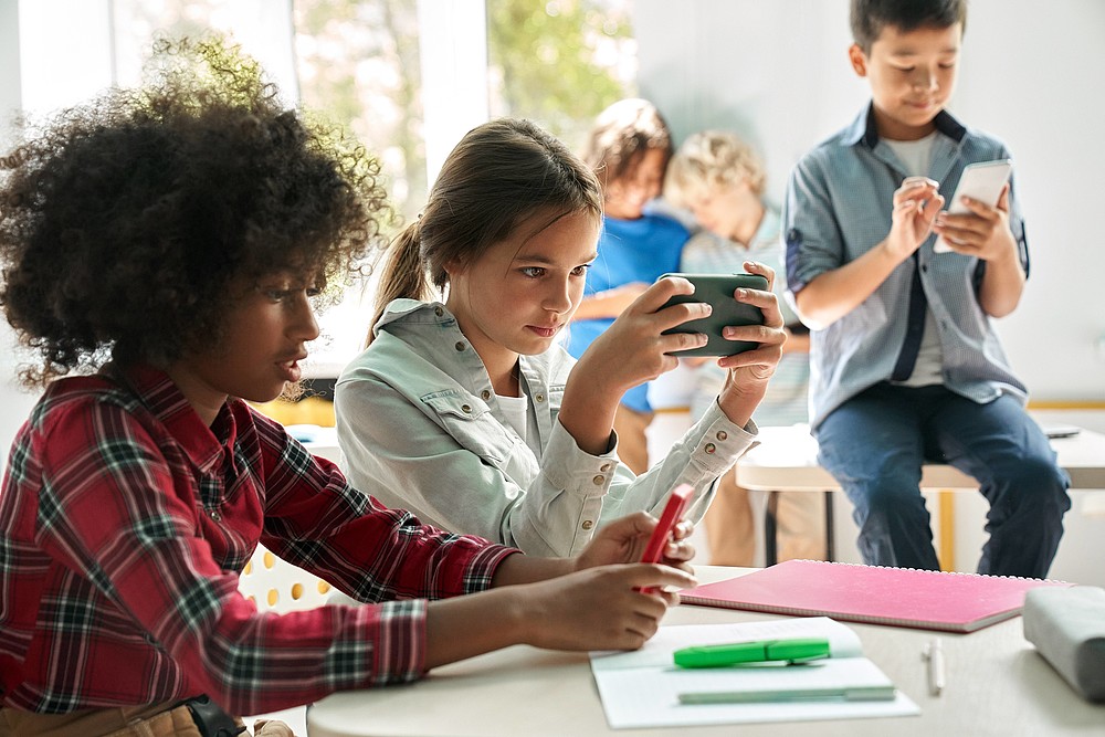 Diverse multiethnic kids school students using smartphones in classroom.