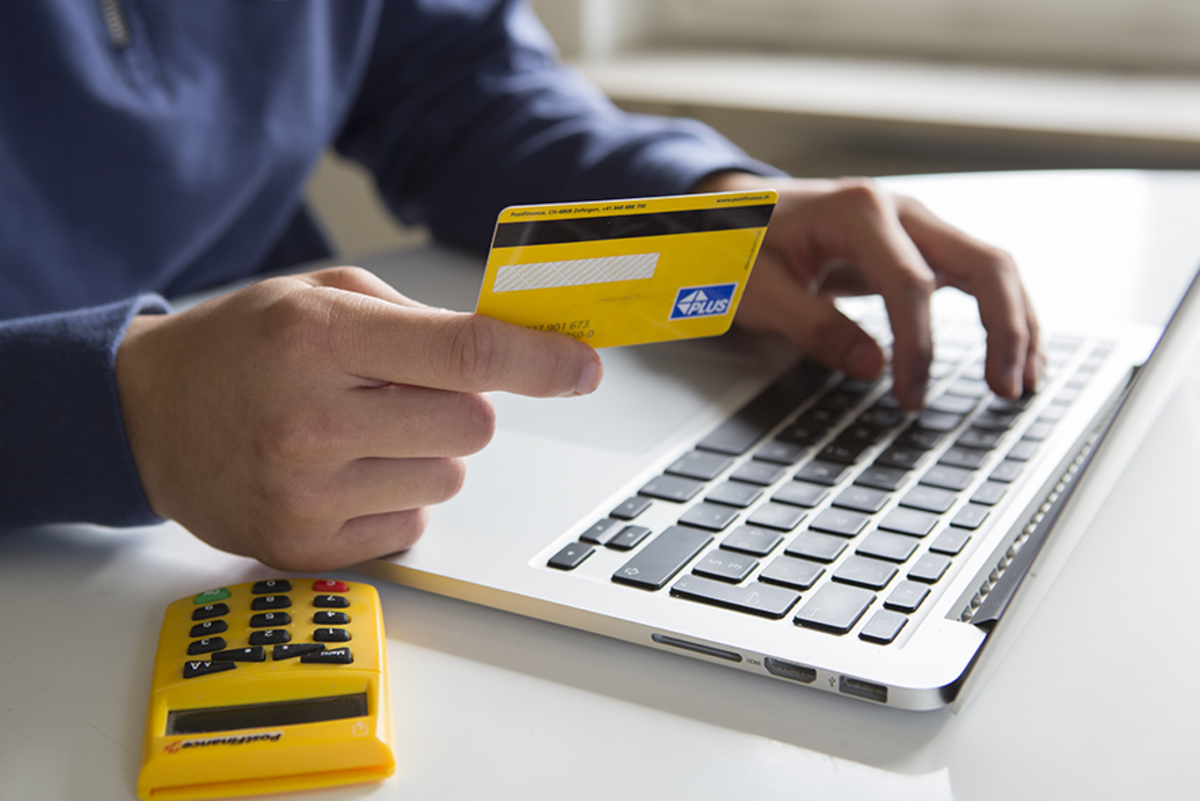 Eine Person die mit einer Bankkarte in der Hand am Laptop Sitzt.