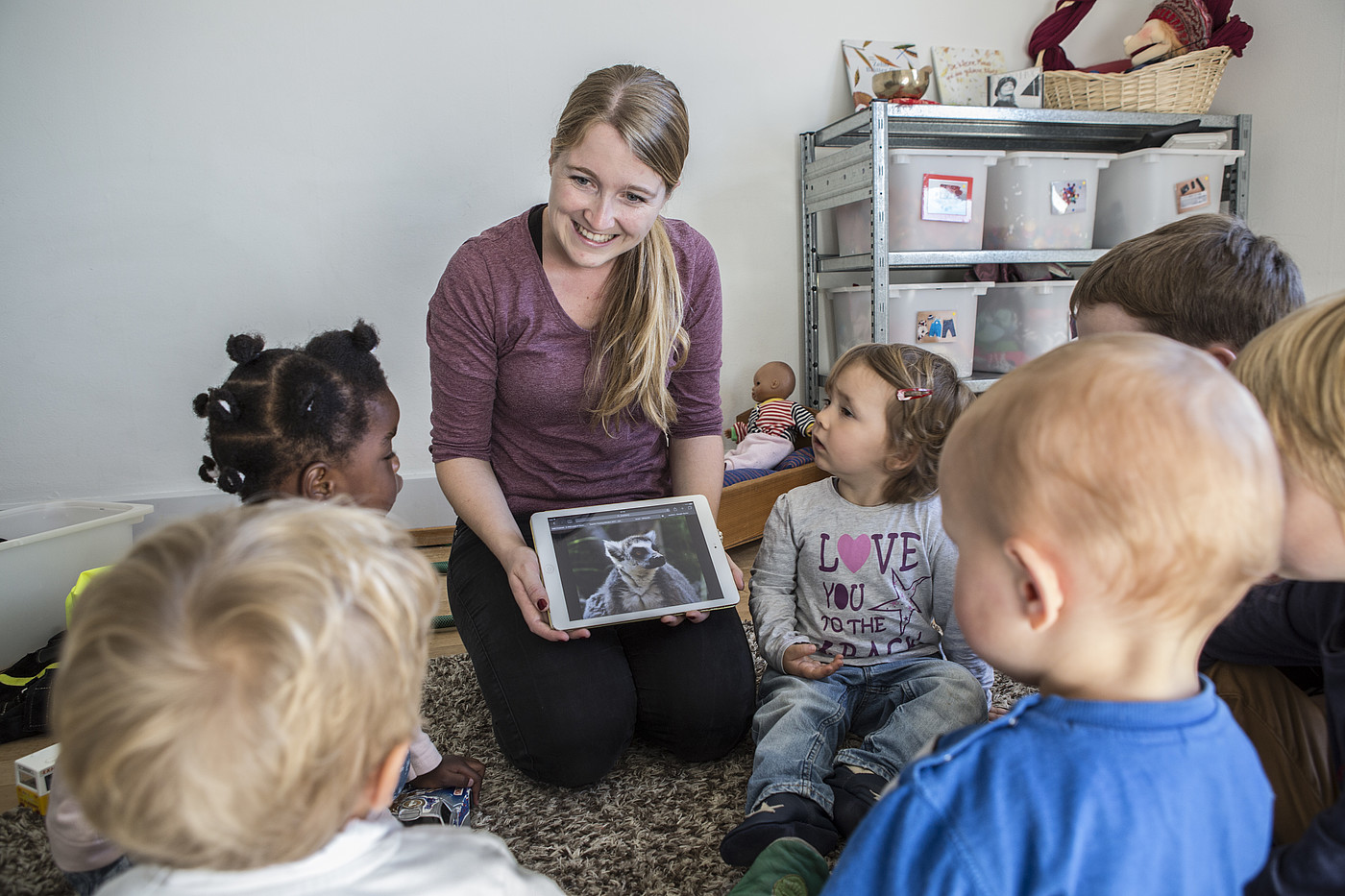 Eine Kinderbetreuerin, welche den Kinder etwas mit dem Tablet erzählt.