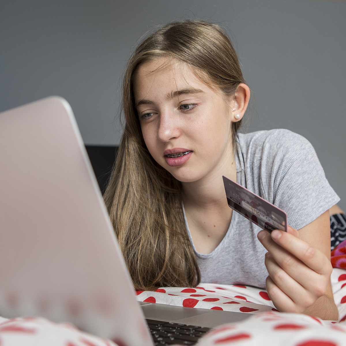 Eine Jugendliche liegt mit dem Laptop auf dem Bett und kauft sich etwas mit der Kreditkarte.