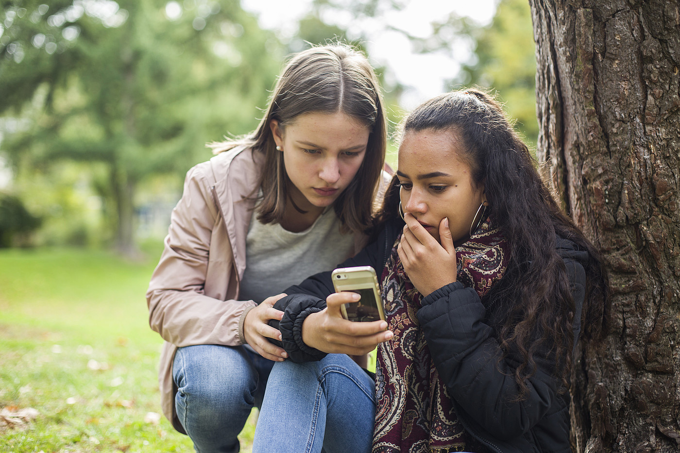 Zwei Jugendliche schauen draussen schockiert auf ein Handy.