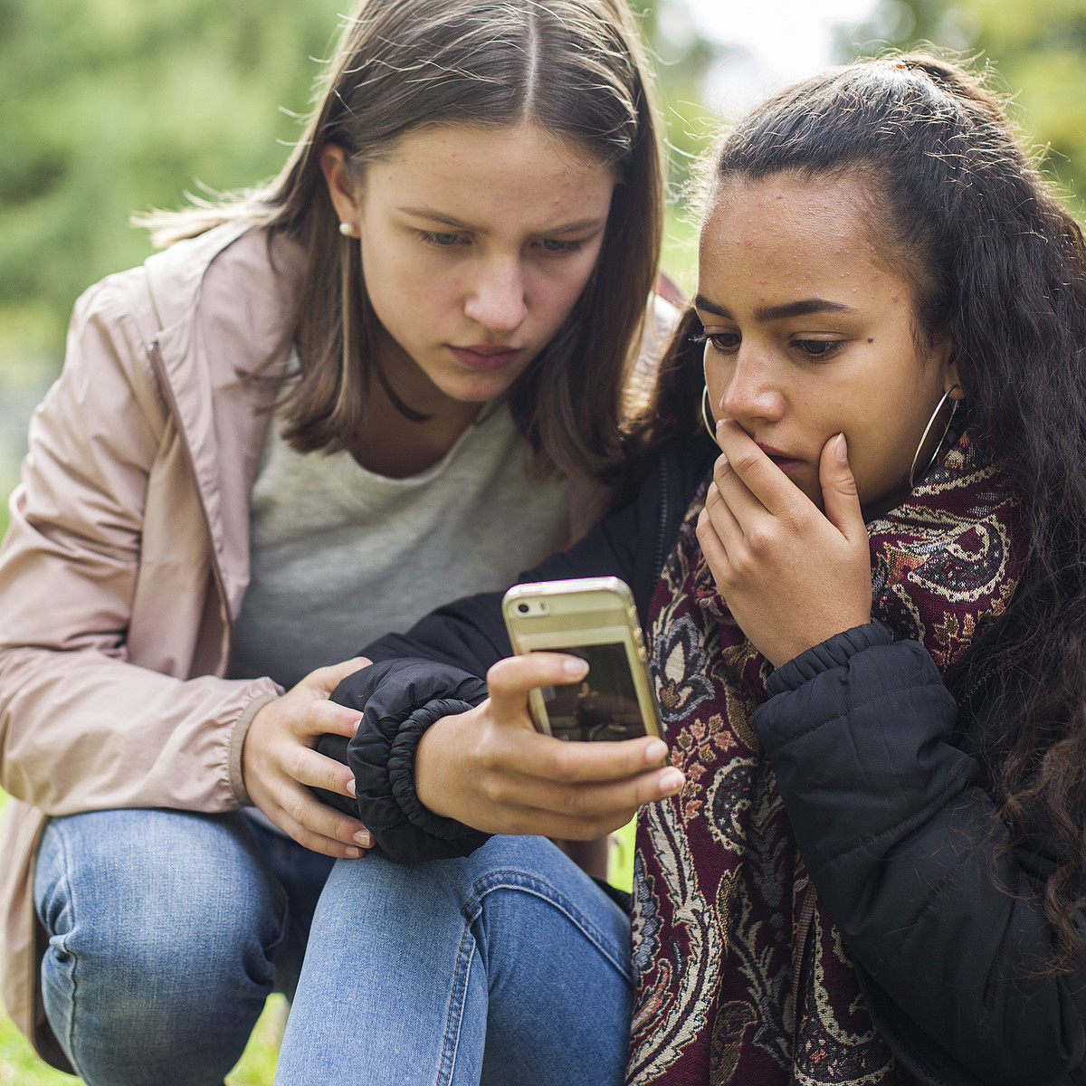 Zwei Jugendliche schauen draussen schockiert auf ein Handy.