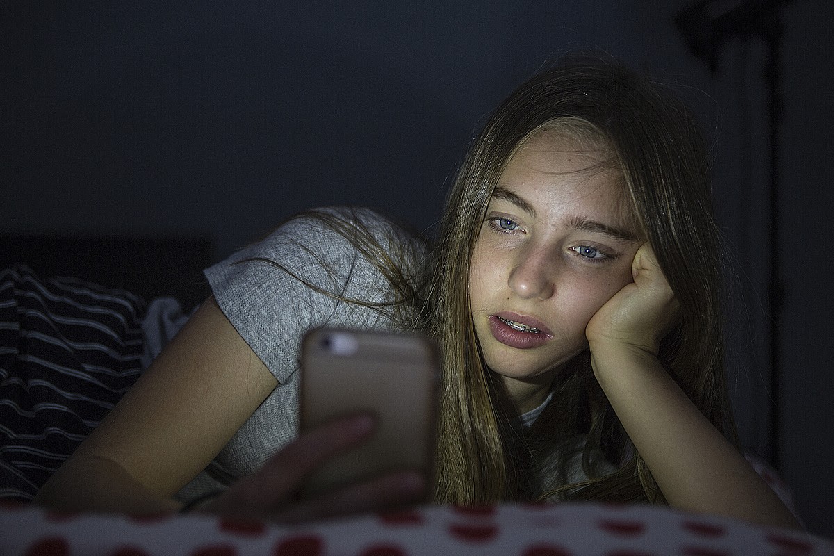 Eine Jugendliche ist liegend im Dunkeln am Handy.
