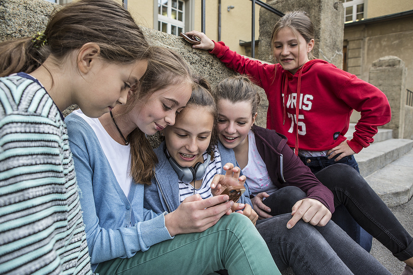 Fünf jugendliche Mädchen schauen draussen auf ein Handy. 