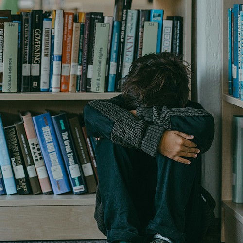 Ein Junge sitzt zusammengekauert in der Bibliothek auf dem Boden. 