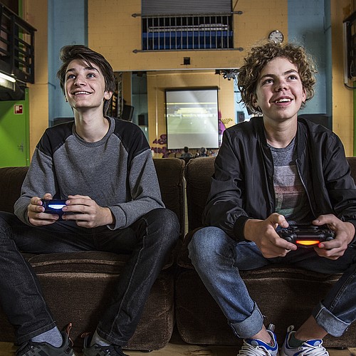Zwei Jugendliche die auf einem Sofa in einem Jugendtreff sitzen und gemeinsam ein Videospiel spielen.