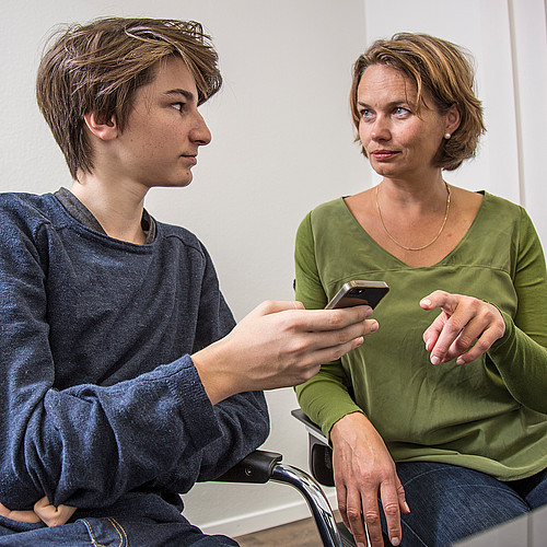 Eine Frau erklärt einem Jugendlichen die Gefahren eines Smartphones. Der Jugendliche hält das Handy selber.