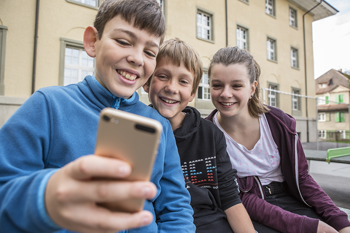Drei Kinder die gemeinsam auf ein Smartphone schauen.